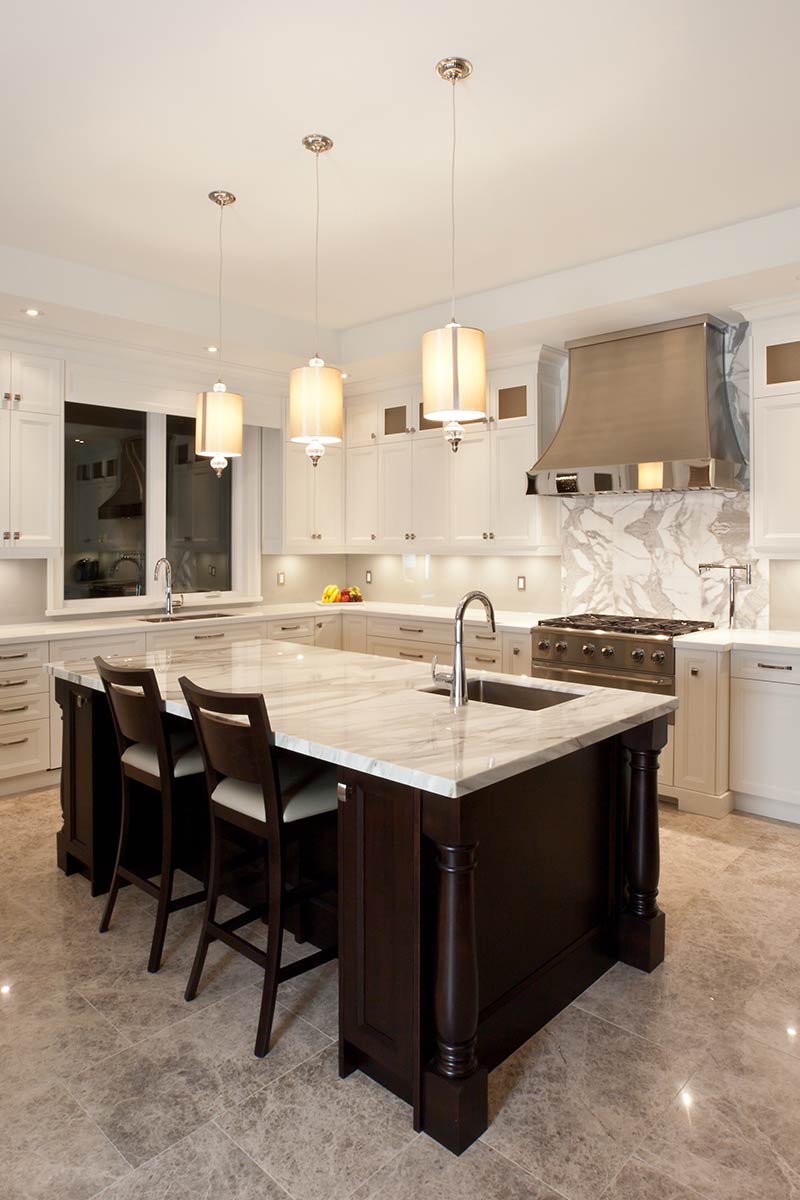 Elegant custom kitchen renovation showcasing light grey cabinetry, wide plank hardwood floors, marble backsplash, and decorative chandelier lighting.